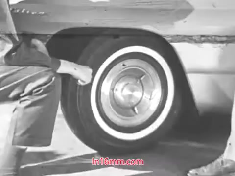 The still features a close-up of a car tire, focusing on the rim and whitewall design. A person, visible from the waist down, is crouching near the tire, likely inspecting it. The overall tone is instructive, emphasizing vehicle safety and maintenance from the 1960s. The context suggests a public service announcement about checking tire wear to promote road safety.