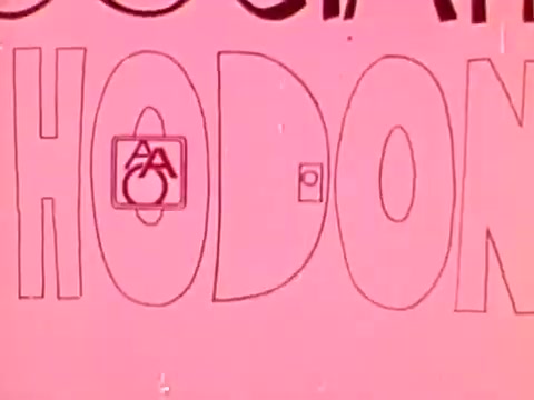 The still features a playful, stylized text with the words 'American Association of Orthodontists' prominently displayed. The letters are bold and rounded, set against a bright pink background. The AAO logo is incorporated into the design, adding a whimsical touch. This highlights the commercial's 1970s aesthetic, characterized by vibrant colors and graphic illustrations. The overall vibe is cheerful and engaging, typical of promotional content from that era.
