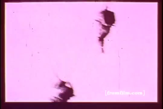 The still from 'Israel Emergency Fund 2 - PSA' features a high-contrast image with a predominantly pink background. It captures two figures in motion, possibly engaged in activities related to the PSA's message. The film exhibits scratches and grain typical of 16mm prints, suggesting a vintage quality. The composition emphasizes the action and urgency associated with the subject matter.