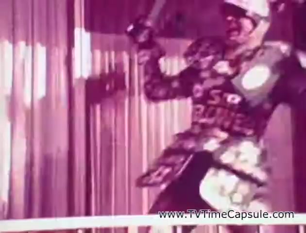 The still from the 'Scott Towel 'Lady Scott'' commercials features a character dressed in a costume decorated with colorful patterns that resemble various paper products, emphasizing the brand's offerings like tissues and paper towels. The setting appears whimsical, with vibrant colors adding to the playful theme of the advertisement. The character seems to be in a dynamic pose, likely engaging viewers with an energetic presentation of the product. The overall aesthetic aligns with mid-20th century commercial styles, aiming to attract attention through bold visuals and creativity.