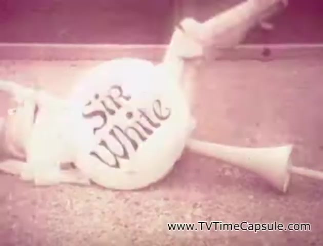 The still features a whimsical character representing a paper product, named 'Sir White.' The character appears to be a rounded, white figure with a playful design and trumpet-like appendages, likely designed to emphasize the softness and quality of the tissue products. The commercial aims to showcase the branding of Lady Scott tissue and paper towels through a light-hearted approach. The visual style suggests a nostalgic quality, typical of vintage advertisements.