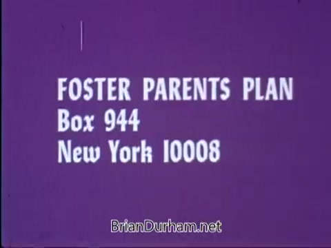 The still features a purple background with bold white text displaying the name 'FOSTER PARENTS PLAN' along with a mailing address: Box 944, New York 10008. It's part of a public service announcement (PSA) featuring the Smothers Brothers, where they discuss adopting overseas children financially through the program. The image emphasizes the call to action for viewers to get involved.