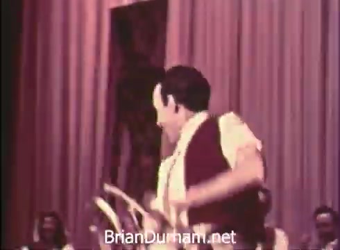 The still from the 'Pittsburgh Folk Festival PSA - 1968' features a performer energetically dancing, likely showcasing folk or cultural dance. The performance takes place on a stage with a backdrop that suggests a festive atmosphere, complemented by the presence of seated audience members visible in the frame. The event is part of the 12th Pittsburgh Folk Festival held at the Civic Arena from June 7th to 9th, presented by Robert Morris Junior College.