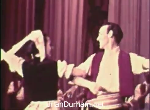 The still from 'Pittsburgh Folk Festival PSA - 1968' features a dance performance, likely showcasing traditional folk dancing. A male and female dancer are in a lively pose, with the male wearing a vest and the female in a dress with a headscarf. The colorful backdrop suggests a festive atmosphere, promoting the 12th Pittsburgh Folk Festival held at the Civic Arena from June 7th to 9th, organized by Robert Morris Junior College.