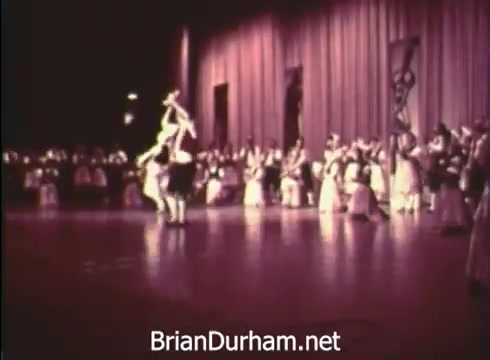 The still from 'Pittsburgh Folk Festival PSA - 1968' captures a performance scene at the event, featuring dancers in traditional attire. The stage is illuminated, showcasing a lively atmosphere with an audience in the background. The festival, presented by Robert Morris Junior College, highlights cultural performances during its 12th edition held at the Civic Arena from June 7th to 9th.