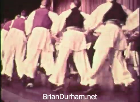 The still features a lively performance at the 12th Pittsburgh Folk Festival in 1968, showcasing dancers in traditional costumes. The performers are in sync, likely engaging in folk dance, with colorful attire that captures the festival's cultural spirit. The setting appears festive, highlighting the event's emphasis on community and heritage.