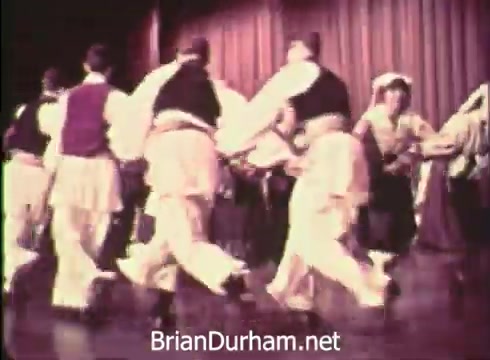 The still from the 1968 Pittsburgh Folk Festival PSA features a lively traditional dance performance. Dancers in colorful costumes are seen engaging in a folk dance on stage, with a vibrant backdrop. The image captures the spirit of cultural celebration, showcasing the diversity and energy of the festival, which took place at the Civic Arena on June 7th, 8th, and 9th.