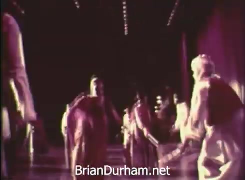 The still from the 'Pittsburgh Folk Festival PSA - 1968' depicts a vibrant performance scene, likely featuring dancers in traditional attire. The background suggests a stage setting, illuminated by bright lights, enhancing the festive atmosphere. This visual serves to promote the 12th Pittsburgh Folk Festival, highlighting the celebration of cultural diversity and folk traditions.
