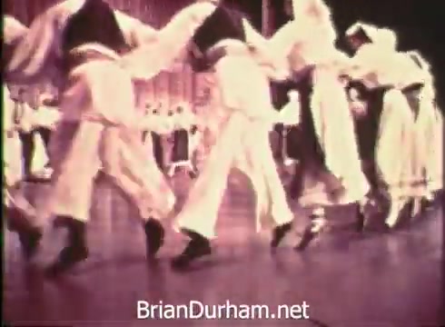 The still from the 'Pittsburgh Folk Festival PSA - 1968' depicts a lively performance featuring dancers dressed in traditional costumes. They are engaged in a synchronized dance, showcasing cultural expressions typical of folk festivals. The backdrop suggests a festive atmosphere, highlighting the event's celebration of diverse cultural heritage, taking place at the Civic Arena from June 7th to 9th.