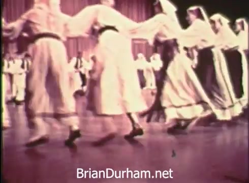 The still from the 1968 Pittsburgh Folk Festival PSA features a traditional dance performance. Dancers, dressed in historical or cultural costumes, are seen linked together in a lively dance, likely celebrating folk traditions. The vibrant atmosphere reflects the festival's focus on cultural expression and community engagement, taking place at the Civic Arena on June 7th, 8th, and 9th.