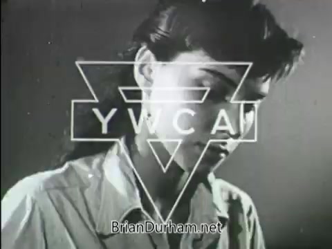 The still features a young woman looking downward, framed by the logo of the YWCA. The image appears to have a monochromatic or muted color style typical of vintage film, emphasizing a serious or contemplative tone. The context suggests it’s part of a public service announcement aimed at promoting the YWCA's mission or services, although the specific date of production is unknown.