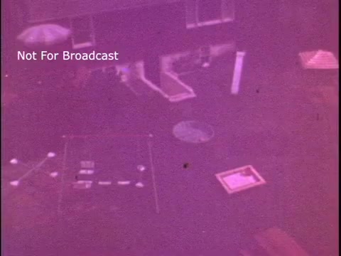 The still from the 'Baggies food storage bag' commercial presents a top-down view of an outdoor setting, possibly a backyard or patio. The image is tinted with a purple hue and features various objects on the ground, including outlines or shapes that suggest organized layouts, likely related to food storage. The overall scene appears to convey themes of organization and functionality, aligning with the product's purpose.