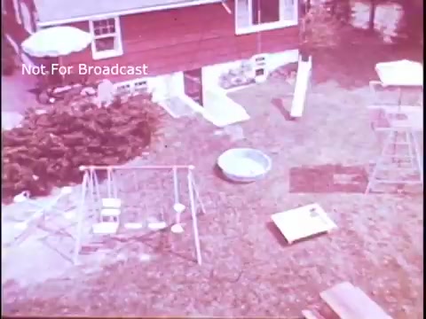 The still captures an aerial view of a backyard, featuring a red house and various outdoor elements. There are swings and a play structure, along with a small pool. The scene evokes a nostalgic, homey atmosphere typical for a family-oriented product advertisement. The overall tone suggests a focus on practical, everyday usage of Baggies food storage bags in a wholesome setting.