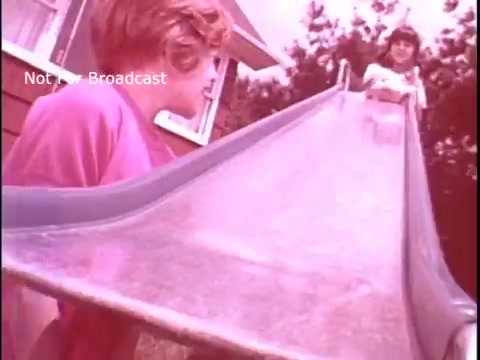 The still features two children at a playground, one at the top of a slide and the other at the bottom, looking up. The image has a vintage feel, with a soft pink hue. The setting suggests a casual, fun atmosphere, typical of a nostalgic family commercial aimed at promoting Baggies food storage bags.