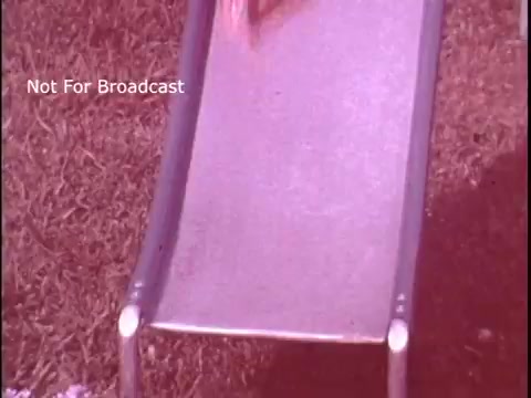 The still features a close-up of a slide, possibly from a playground, with grass visible beneath it. The image has a warm, slightly faded tone typical of 16mm film. There is no visible action or characters, creating a nostalgic and playful atmosphere, likely aiming to evoke a sense of childhood fun related to the commercial's theme of food storage. The watermark “Not For Broadcast” indicates it is not meant for public airing.