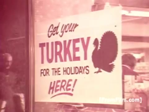 The still features a vintage promotional sign advertising 'TURKEY FOR THE HOLIDAYS HERE!' The sign is visually prominent, with a graphic of a turkey beside the bold lettering. The setting suggests a market or grocery store, typical of the 1970s. The overall tone is nostalgic, reflecting the era's advertising style and Frank Perdue's focus on quality poultry products.