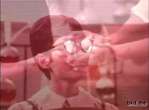 The still from the 1970s Camay Soap commercial features a young boy wearing glasses, appearing curious or surprised. He is in a laboratory-like setting, with a hand (presumably an adult) reaching towards him, possibly demonstrating something related to the product. The overall aesthetic is soft with a vintage film grain, characteristic of 16mm prints from that era. Bright colors and playful elements may suggest a lighthearted approach to promoting the soap.