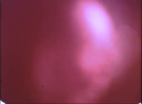 The still from the trailer of 'A Reflection of Fear' features a blurred, hazy background with a predominately reddish hue, typical of a vintage 16mm print. The lack of clear imagery adds to the eerie atmosphere, suggesting a sense of confusion or dread, fitting for a horror genre. The overall quality reflects its age, enhancing the nostalgic feel for fans of classic horror films.