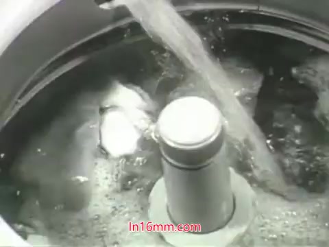 The still from the PSA features a close-up of a washing machine in action. Water is flowing into the machine, creating bubbles and movement, suggesting a cleaning process. This imagery aligns with the voiceover by Mason Adams, which emphasizes the contrast between washing soiled items and the inability to wash one's lungs from pollution. The focus on the washing machine serves as a metaphor for the broader message about urban air quality challenges in the 1960s. Overall, it conveys a strong public health message urging viewers to take action for cleaner air.