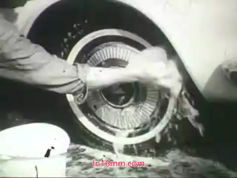 The still features a close-up of a person washing a car wheel, emphasizing the need for cleanliness in the context of urban air pollution. The hands are actively scrubbing away dirt and grime, symbolizing the broader message about maintaining health in polluted environments. The visuals contrast the idea of washing physical surfaces with the inability to cleanse lungs from polluted air, as stressed in Mason Adams' voiceover. The imagery reinforces calls to action regarding public health and air quality awareness.
