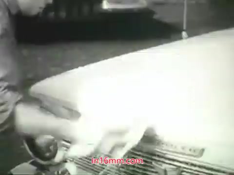 The still captures a man washing the hood of a car, highlighting the theme of cleanliness in the context of urban air pollution. The man is actively scrubbing the vehicle, indicating an effort to remove dirt and grime. Accompanying this visual is a voiceover by Mason Adams that emphasizes the inability to clean one's lungs from the pollutants present in city air. The message is a call to action, urging viewers to contribute towards improving air quality in their communities. The tone reflects a public service announcement aimed at raising awareness about environmental health issues in the 1960s.