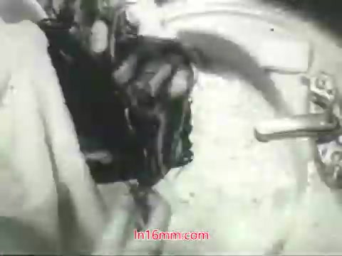 The still from the PSA features a close-up shot of a hand washing a soiled item—likely a piece of clothing or fabric—inside a round basin or sink. The image is in black and white, characteristic of 1960s film, emphasizing the action of cleaning. The context of the voiceover by Mason Adams discusses urban air pollution, suggesting that while many objects can be washed to remove dirt and grime, lungs cannot be cleaned in the same way, highlighting the importance of addressing air quality. The overall tone conveys a public health message urging viewers to take action for cleaner air.