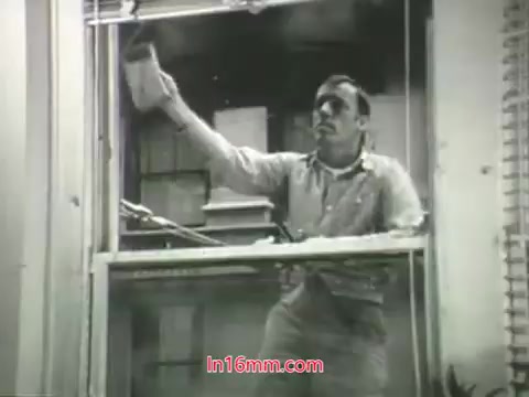 The still from the PSA features a man cleaning a window from the inside of a building. He is dressed casually and appears focused on his task. The scene conveys a sense of the struggle with pollution, emphasized by the voiceover from Mason Adams discussing the challenges of urban air quality. This visual complements the message that while many surfaces can be cleaned, our lungs cannot be washed, urging viewers to consider actions to improve air quality. The overall tone suggests a call to awareness and action related to public health and environmental responsibility.