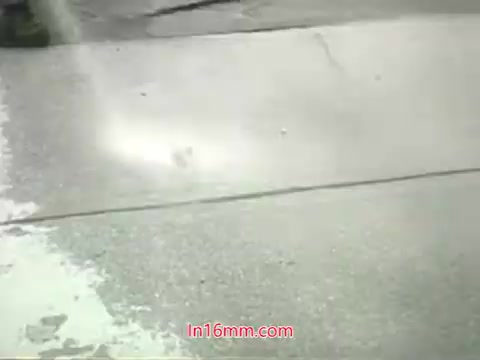 The still from the PSA features a city street, likely showing a person or machine washing down the pavement, illustrating efforts to combat pollution. The visuals support the narrative by highlighting urban cleanliness amidst environmental issues. The voiceover by Mason Adams emphasizes the importance of addressing air pollution, pointing out that while we can clean surfaces, our lungs remain vulnerable. The message encourages action for cleaner air, urging viewers to engage with local initiatives.