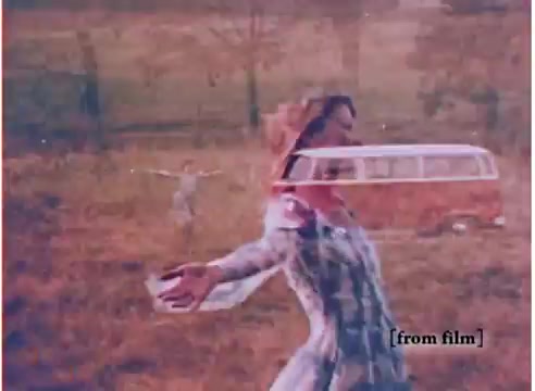 The still from the 1973 Volkswagen station wagon commercial features a woman in a carefree pose, arms extended, standing in an open field. In the background, a vintage Volkswagen bus is visible, slightly overlaid with a ghostly effect. The overall tone is nostalgic, emphasizing a sense of freedom and leisure associated with the vehicle. The colors are warm and somewhat muted, reflective of the 1970s style.