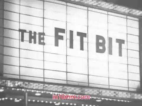 The still features a vintage marquee sign displaying 'THE FIT BIT.' It's likely part of a 1960s advertisement for Leg Street panty hose, emphasizing fit and style. The context suggests a catchy jingle promoting the convenience and affordability of their panty hose, appealing to consumers seeking fashionable options. The retro aesthetic reflects the era's marketing style.