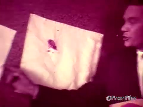 In the 16mm still from the Tide XK laundry detergent commercial, a man points to a white guest towel exhibiting a noticeable stain, likely representing blood. He speaks of the potential shock from such a stain, implying it would cause distress ('Blanche will flip'). Another segment highlights a ketchup stain on a different towel, emphasizing the effectiveness of the new Tide XK detergent by declaring that it breaks through tough stain barriers. The overall theme underscores Tide XK's advanced cleaning capabilities for seemingly impossible stains.