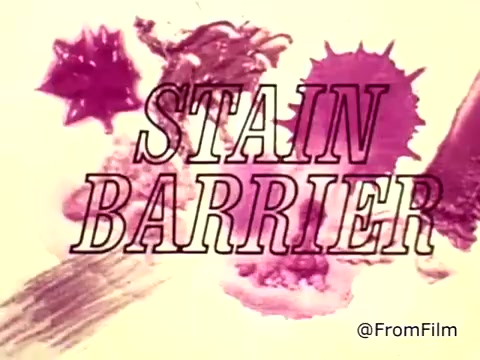 The still features bold text stating 'STAIN BARRIER' prominently displayed against a backdrop of vibrant, colorful stains, likely representing ketchup and blood. The visual emphasizes the theme of overcoming tough stains, suggesting a breakthrough in cleaning technology with Tide XK laundry detergent. The context indicates concerns about difficult stains in a household setting, highlighting the product's effectiveness.
