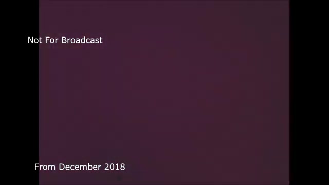 The still presents a frame labeled 'Not For Broadcast' along with a date 'From December 2018.' It likely pertains to the archival footage of a discussion regarding the transfer of a TV commercial, specifically involving the technical challenges and processes needed to convert film to video. The color background sets a professional tone, while the context indicates a focus on historical or production-related insights that were previously unpublished, possibly due to audio sync issues that have since been addressed.