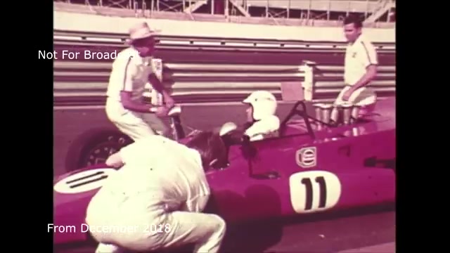 The still from the December 2018 transfer talks features a vintage 16mm film frame depicting a scene at a racetrack. It captures a moment where a team appears to be working on a race car, prominently displaying the number 11. Several individuals, dressed in white attire, are engaged in what looks like a pit stop or maintenance task. The setting suggests a dynamic racing environment, likely during the era when film commercials were transitioning to video formats. You highlight the audio sync issues you faced, which you have since addressed.