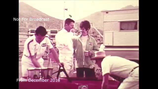 This 16mm still from the 'Chase and Sandborn Commercial' depicts a lively outdoor scene, likely during a film shoot from the late 1960s or early 1970s. Several individuals are engaged in activities around a red vehicle, with a relaxed atmosphere. One person appears to be conversing with a woman who is holding a beverage, suggesting a casual yet collaborative spirit. The presence of a trailer in the background indicates a production setup. Your mention of audio sync issues highlights technical challenges you encountered during the transfer from film to video, which you have since addressed.