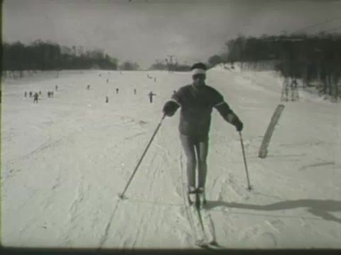 The still depicts a skier in a snowy landscape, emphasizing skiing safety. The skier is in a casual stance, using ski poles, with a snow-covered slope and other skiers visible in the background. The scene conveys a sense of winter recreation.