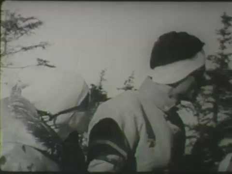 The still from the Aetna public safety message features two skiers dressed in winter attire, including headbands and jackets. They are situated outdoors, likely on a ski slope, with snow-covered trees in the background. The image conveys a sense of winter sports activity and emphasizes safety in skiing. The black-and-white format suggests it is from an earlier era, highlighting the timelessness of safety messages in outdoor sports.