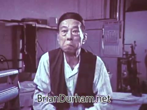 The still from the 1968 'Another Red Rose Tea' commercial features a man with an expressive face, likely conveying a humorous or surprised reaction. He is dressed in a simple outfit and appears to be in a workshop or studio setting. The overall tone suggests a light-hearted promotion for Red Rose Tea, potentially highlighting its taste or quality through comedic elements.