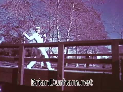 The still from the 1968 Red Rose Tea commercial features a performer in a sailor outfit, dancing on a wooden bridge. The scene is set against a backdrop of bare trees, suggesting a springtime or early summer atmosphere. The visual style reflects the vibrant colors typical of that era, capturing a playful, cheerful vibe appropriate for a tea advertisement.