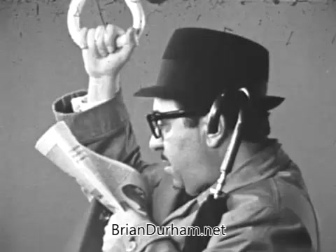 The still from the 1968 PSA 'Get Yourself Tested for Diabetes' features a man wearing a black hat and glasses, holding a newspaper in one hand and an object resembling a handle in the other. His attire suggests a vintage style typical of that era, and he appears somewhat contemplative, conveying a sense of concern regarding health. The voiceover links the visuals to a discussion about diabetes awareness, particularly emphasizing the importance of testing for those over 40 and possibly overweight.