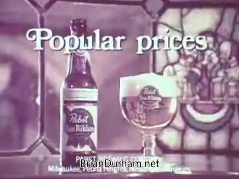 The still features a classic Pabst Beer advertisement highlighting 'Popular prices.' It displays a Pabst beer bottle next to a glass filled with the beer, showcasing the brand's logo prominently. The background includes stained glass elements, adding to the vintage aesthetic of the commercial. The overall design emphasizes affordability and quality, characteristic of mid-20th century beer marketing.