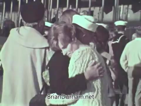 The still depicts a scene of emotional reunion, showing two women embracing amidst a crowd, likely of sailors in uniform. The environment suggests a naval setting, possibly at a port or base. The women appear to share a moment of connection, reflecting themes of support and familial bonds related to military service.