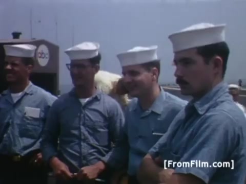 The still from 'Western Union International - prep for Apollo 11' features a group of sailors wearing matching light blue uniforms and white hats. They appear engaged and attentive, likely in anticipation of the satellite transmission process related to Apollo 11's recovery operation via the USS Hornet. Their expressions convey a sense of pride and focus, reflecting the significance of the event.