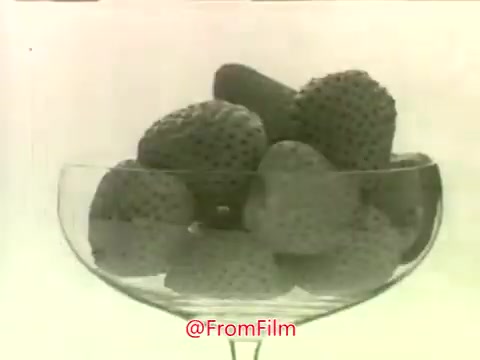 The still features a glass bowl filled with strawberries, prominently displayed against a simple background. The black-and-white film captures the strawberries’ texture and shape. This imagery aligns with the promotional theme of the Dream Whip dessert topping, likely showcasing its use with fresh fruits for desserts in a classic 1960s commercial style.