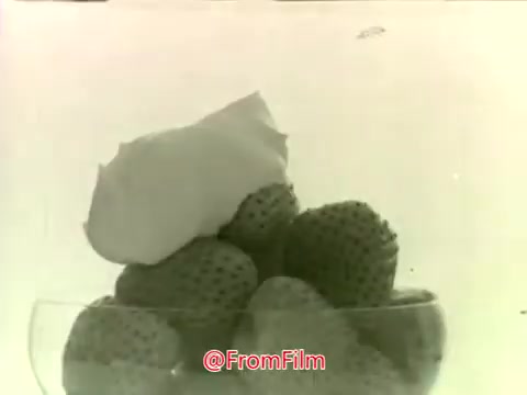 The still from the 'Dream Whip Commercial - 1960s' showcases a bowl filled with strawberries topped with a generous swirl of Dream Whip dessert topping. The black-and-white format gives it a vintage feel, characteristic of that era's advertising style. The focus is on the appealing presentation of the strawberries and the creamy topping, highlighting the product's use as a dessert enhancer.