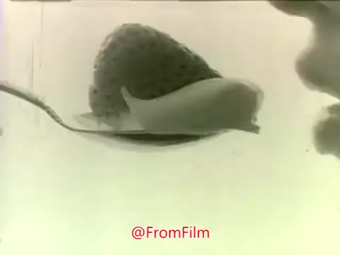 The still features a close-up shot of a spoon with a dollop of Dream Whip dessert topping placed atop a mound of strawberries. The image has a soft, faded quality typical of 16mm film from the era, with a light background that emphasizes the enticing texture of the topping and the fruit. The composition highlights the creamy texture of the Dream Whip, reinforcing its appeal as a dessert topping in the commercial context.