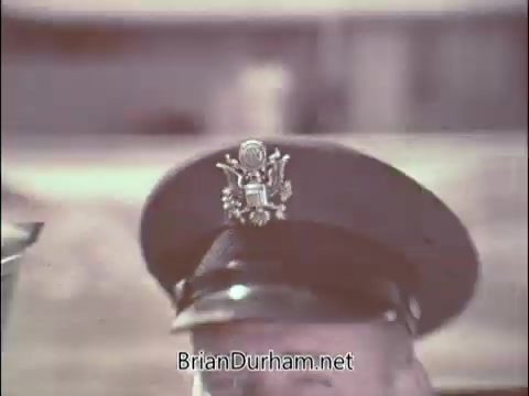 The still depicts a close-up of a military cap, specifically an Air Force officer's hat featuring insignia. This image likely connects to a 1960s PSA aimed at recruiting doctors for the Air Force Reserve during the Vietnam War. The cap symbolizes authority and military service, aligning with the ad's intentional appeal to medical professionals.
