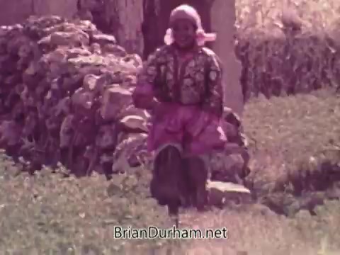 The 16mm still from the 1972 Coca-Cola Olympics commercial features a woman in traditional clothing, energetically running through a rural landscape. Stone walls and greenery set the backdrop, capturing a sense of vitality and cultural essence. The commercial, created during a tumultuous time in Olympic history, aimed to convey themes of unity and celebration.