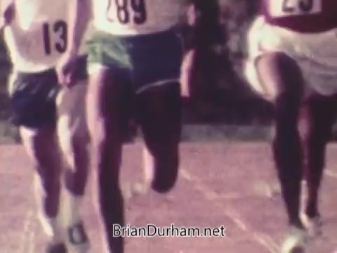 The still from the 1972 Coca-Cola commercial shows athletes in competitive running gear, focusing on their legs as they sprint on a track. The image captures the urgency and energy of the race, emphasizing athleticism against the backdrop of the 1972 Munich Olympics, a games marked by both sporting excellence and tragedy.