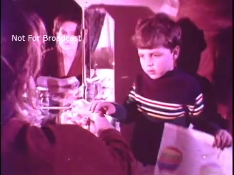 The still depicts a young boy in a striped sweater interacting with an unseen adult, likely a caregiver, as they share a moment over a colorful drawing. The setting has a warm, nostalgic feel typical of the 1970s. In the background, a reflective surface suggests an intimate, domestic environment, emphasizing themes of connection and mental well-being. The overall tone is serious, aligning with the PSA's focus on mental health awareness.